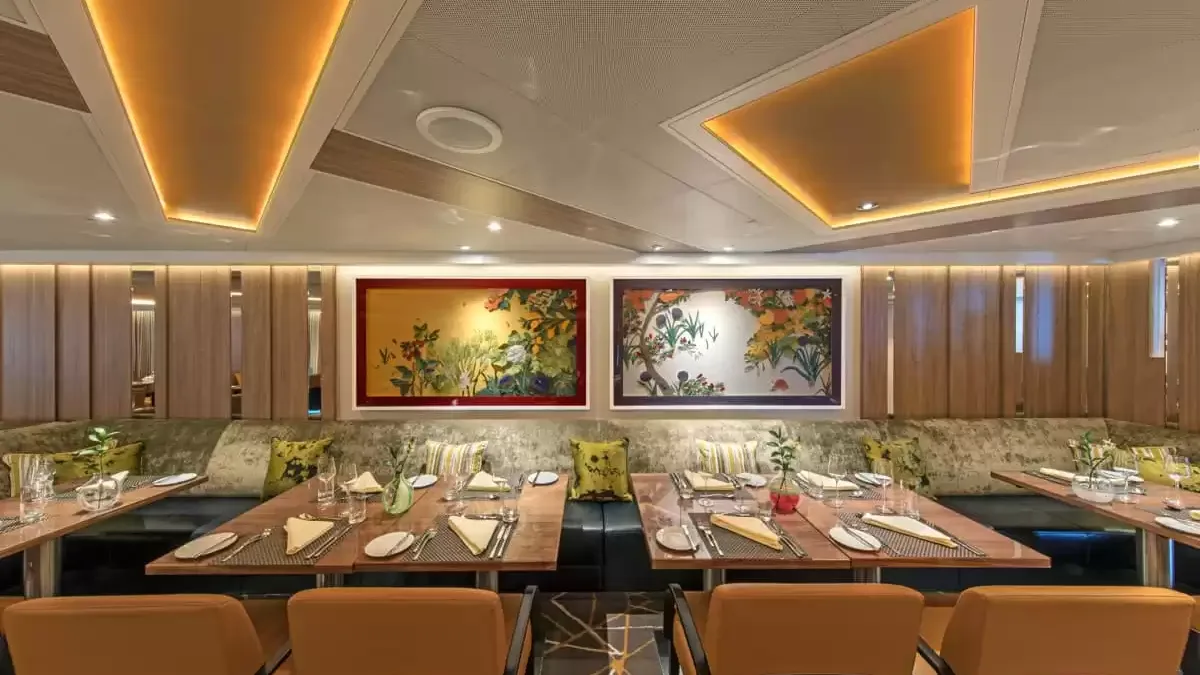 Salle de restaurant du Seabourn Ovation, tables en bois sous deux peintures florales