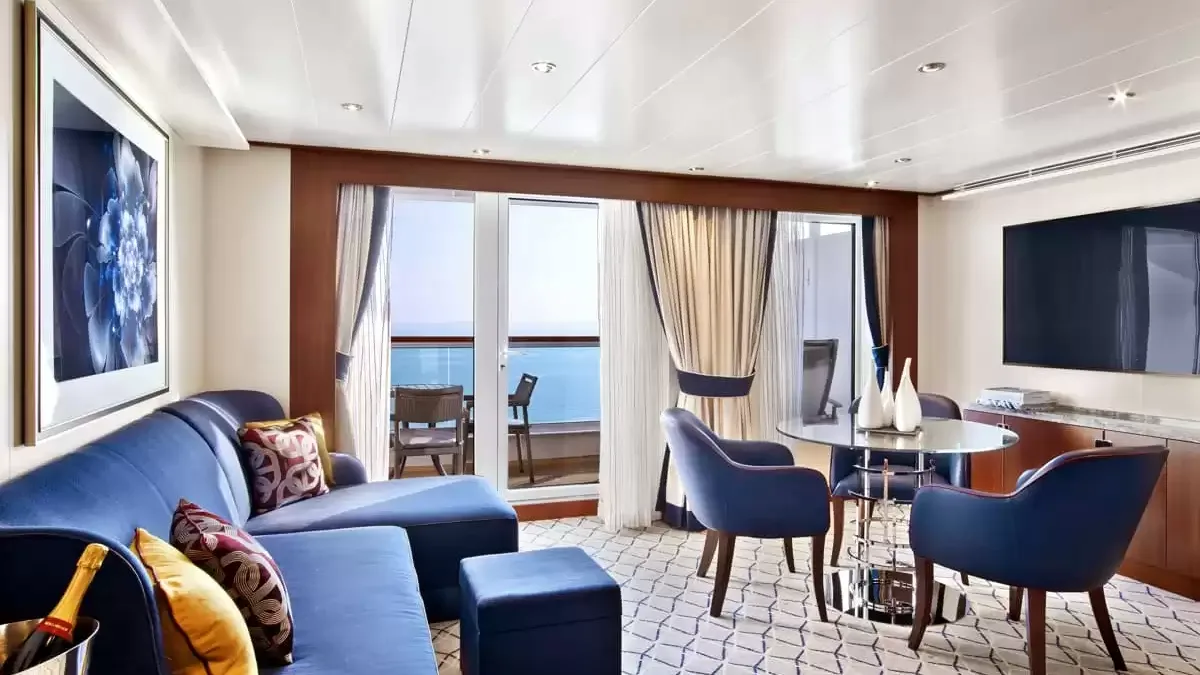 Salon d’une suite du Seabourn Ovation, canapé bleu, coin repas et balcon sur la mer